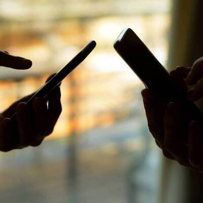 Silhuett av två personers händer som håller i mobiltelefoner.