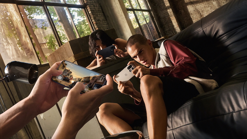 Personer som spelar mobilspel tillsammans i en ljus industriell lokal med stora fönster och lädersoffor.