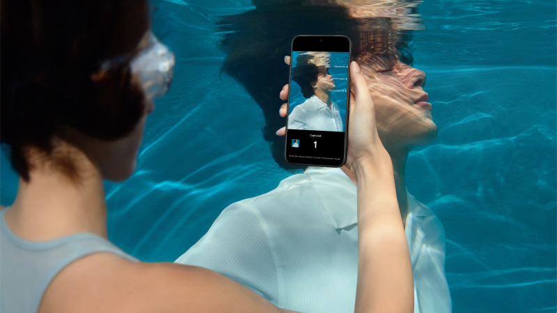 Person under vatten tar en bild med vattentät smartphone i turkosblått poolvatten.