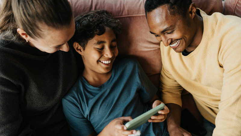 En kvinna, en man och en pojke sitter i en soffa och tittar på en mobiltelefon.