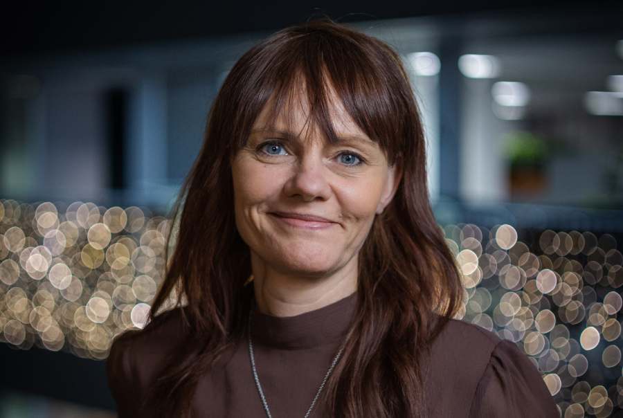 Pernilla Hassel, Account Manager på Tele2 Företag. Hon är klädd i en vinröd blus och har brunt hår. Bakom henne skymtar ett kontorslandskap med ljusslingor över ett räcke.