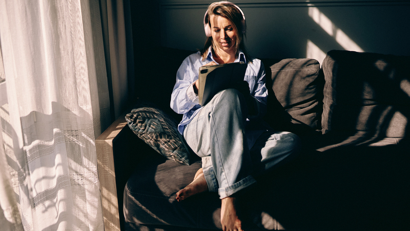 En kvinna sitter i en soffa med hörlurar och ett anteckningsblock.