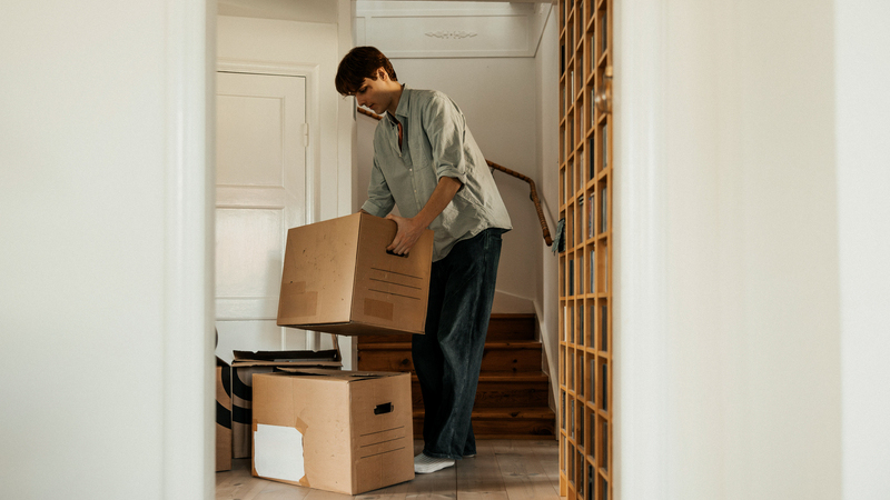 En man bär flyttkartonger i en bostad.