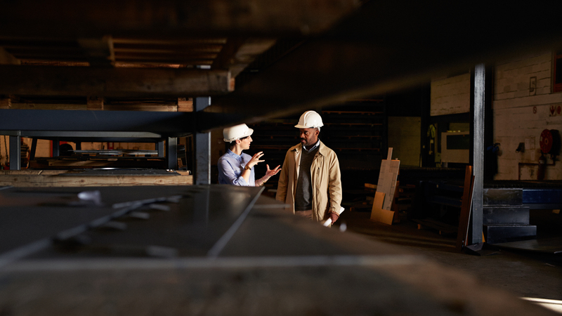 En man och en kvinna i hjälmar fotograferade på avstånd på ett fabrikslager.