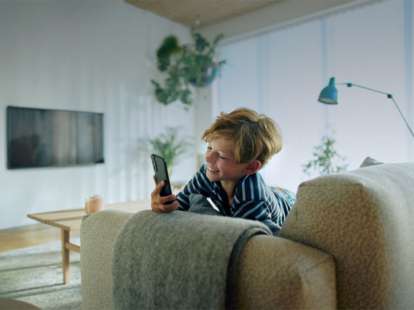 Pojke sitter i soffan med mobilen i handen