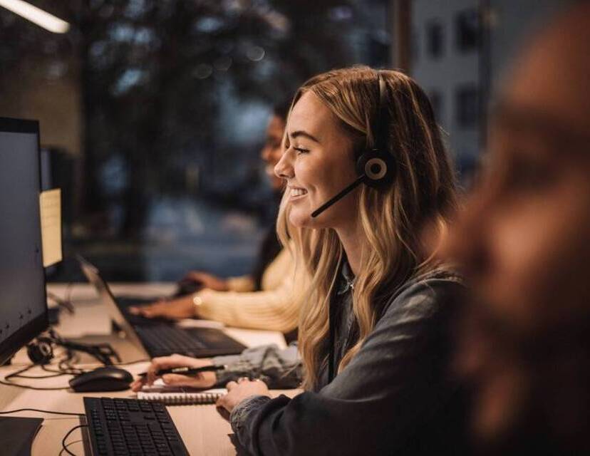 Profilbild på kvinna med headset som sitter framför en datorskärm.