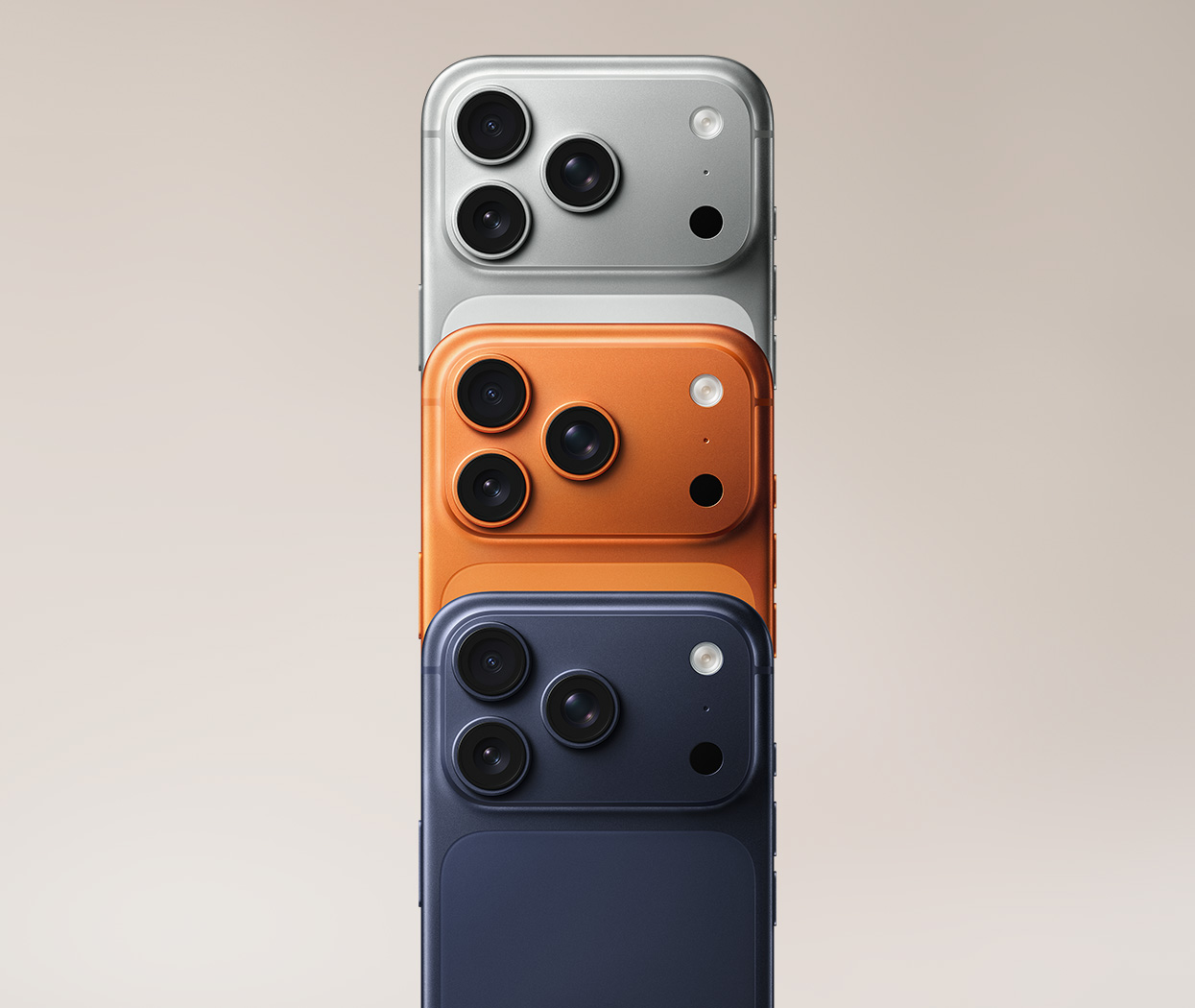 Tre smartphones staplade bakåt i färgerna silver, orange och mörkblå, med trippelkameror synliga på varje enhet.