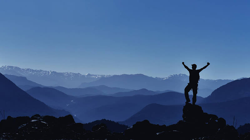 Man som sträcker ut armarna på toppen av ett berg