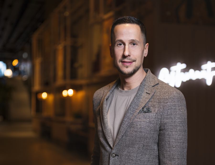 Andreas Komada, vd för företaget Tolerate som tillverkar miljövänliga mobilskal, småleende och klädd i en brunrutig kavaj och brun t-shirt. I bakgrunden syns husfasader och upplysta skyltar.