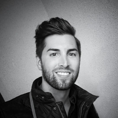 Svartvit porträttbild av Philip Entesarian, Account Manager på Tele2 Företag. Han har mörkt hår och kort skägg och ler. Han är klädd i en mörk jacka och står framför en ljus vägg.