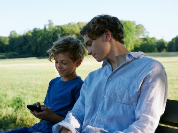 Två bröder som sitter på en parkbänk och kollar tillsammans i en mobil
