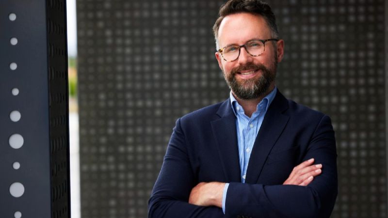 Tele2s hållbarhetschef Erik Wottrich står framför en husvägg, leende och klädd i kavaj och skjorta.