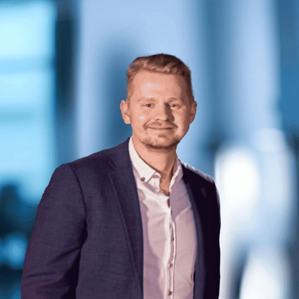 Henric Persson, Account Manager på Tele2 Företag. Han står vänd mot kameran och är klädd i mörkblå kavaj och vit skjorta. Han har ljust hår och kort skägg och ler. I bakgrunden skymtar ett kontor i blå toner.