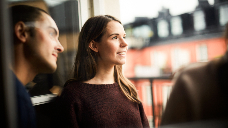 En man och en kvinna står vid ett fönster i en stad med hus i bakgrunden.