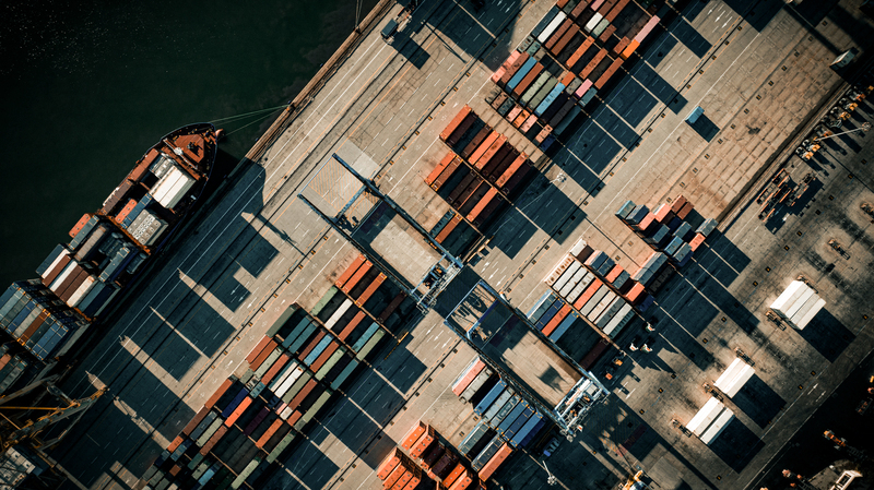 Vy ovanifrån över en industrihamn med lastfartyg och kontainrar.