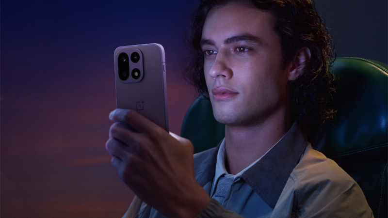 Person med lockigt hår tittar på en smartphone i ett mörkt rum med lila belysning, sittande i en grön stol.