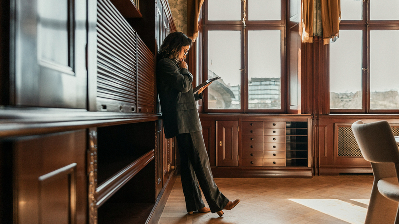 En kvinna står lutad mot en vägg på ett kontor och läser på ett papper.