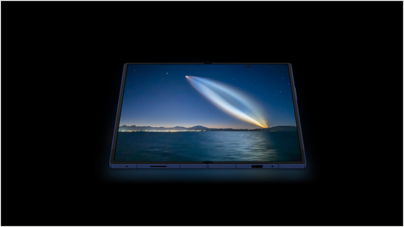 En Samsung Galaxy Z Fold7 som visar en natthimmel med ett ljust komet eller meteor över ett mörkt hav med avlägsna ljus vid horisonten.