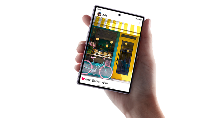 En hand håller en smartphone som visar ett socialt medieinlägg med en rosa cykel framför en gul butik.