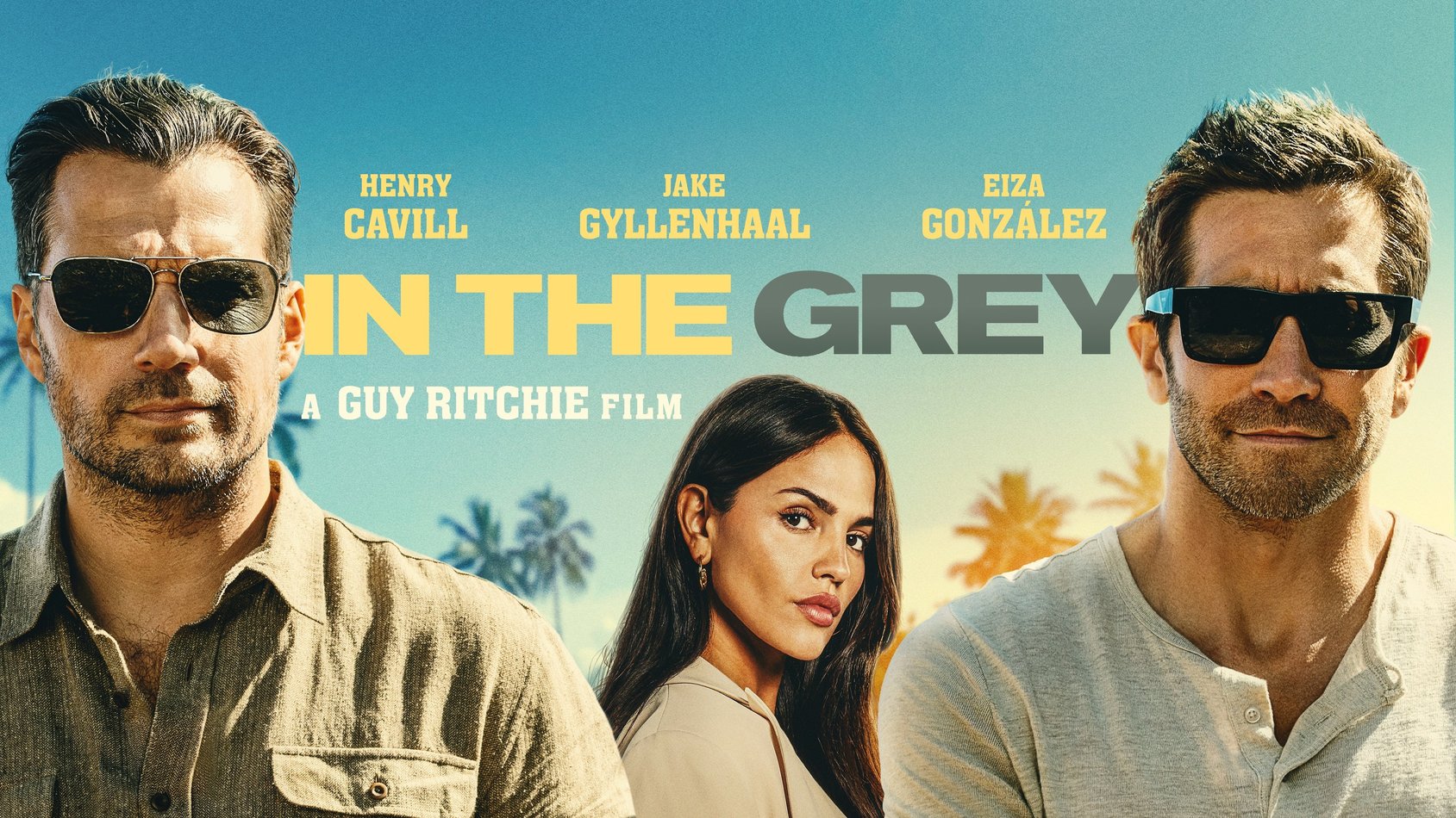 Filmaffisch för "In The Grey" med Henry Cavill, Jake Gyllenhaal och Eiza González mot en solig bakgrund med palmträd.
