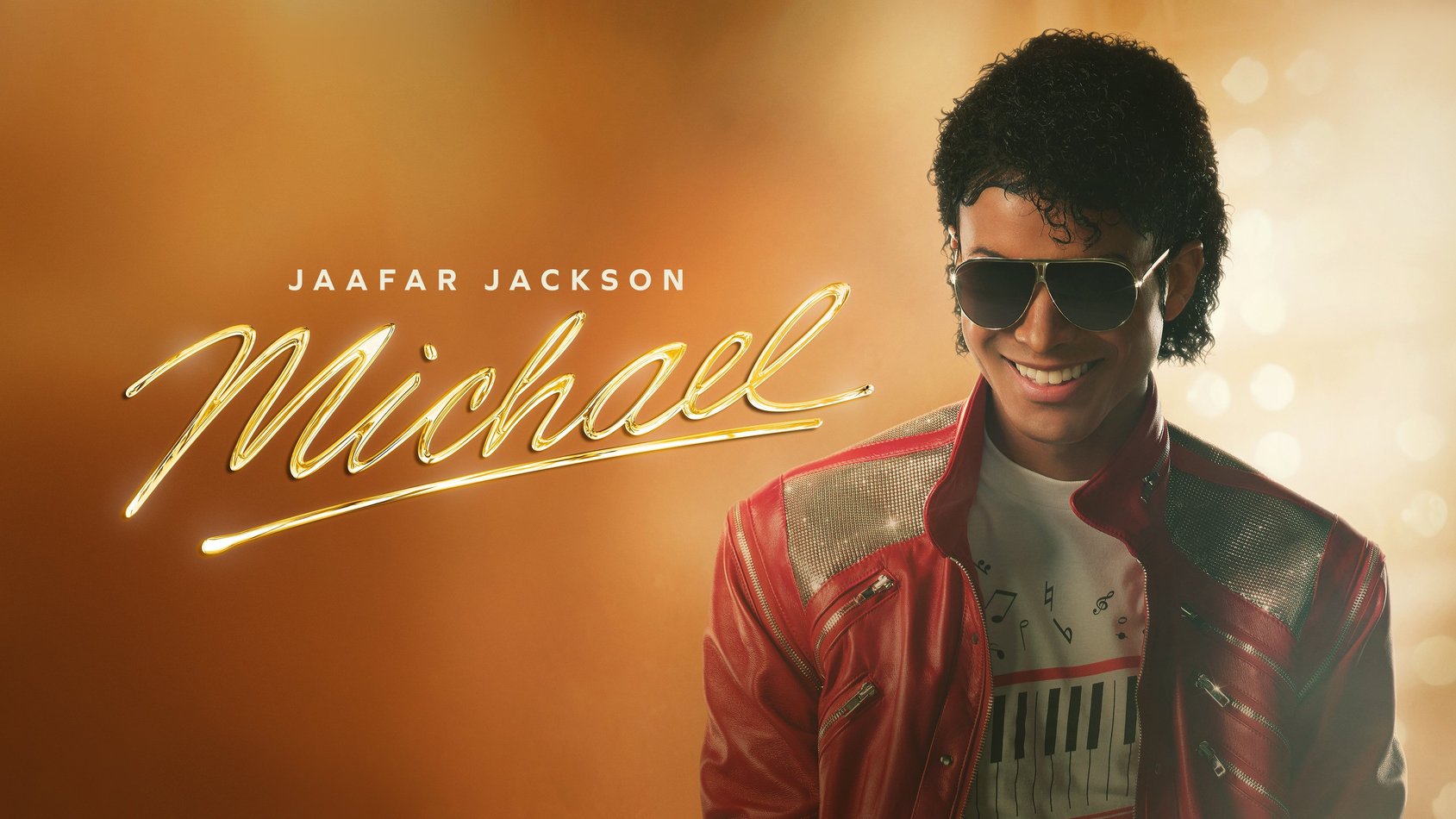 Jaafar Jackson ler i röd jacka och solglasögon mot gyllene bakgrund med texten "Michael" i guld.