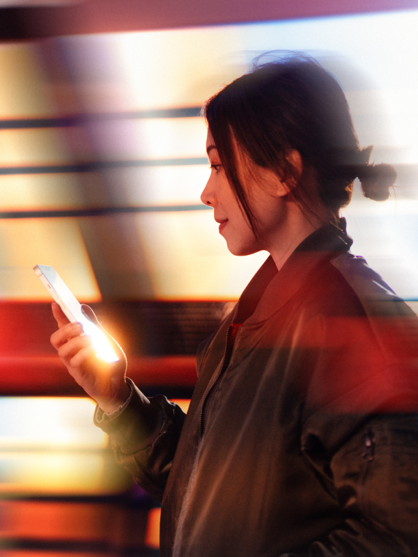 Person i profil tittar på lysande mobiltelefon mot bakgrund av suddiga färgglada ljus i rörelse.