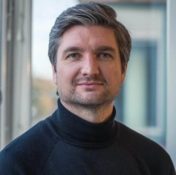 Anders Grape, it-servicedeskansvarig på Fonus. Han har grått hår och svart polotröja och står framför ett fönster med andra byggnader i bakgrunden.