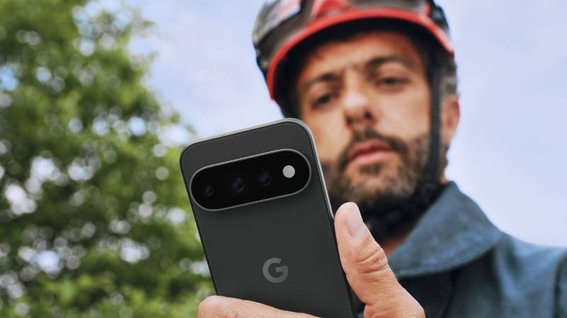 Man med hjälm och arbetskläder som tittar på en smartphone. Mobilen har svart baksida och kamera högst upp samt en logotyp med bokstaven G.