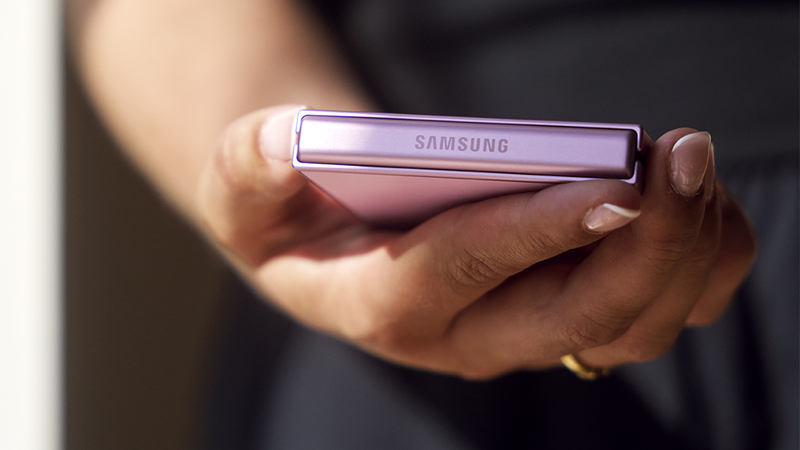 Närbild på hand som håller en hopvikt smartphone med rosa baksida.