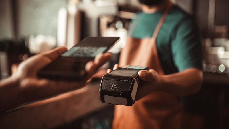 Närbild av person som håller fram en mobiltelefon mot en betalterminal på restaurang.
