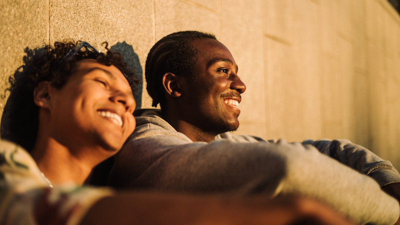 En man och en kvinna sitter lutade mot en husvägg i solen.