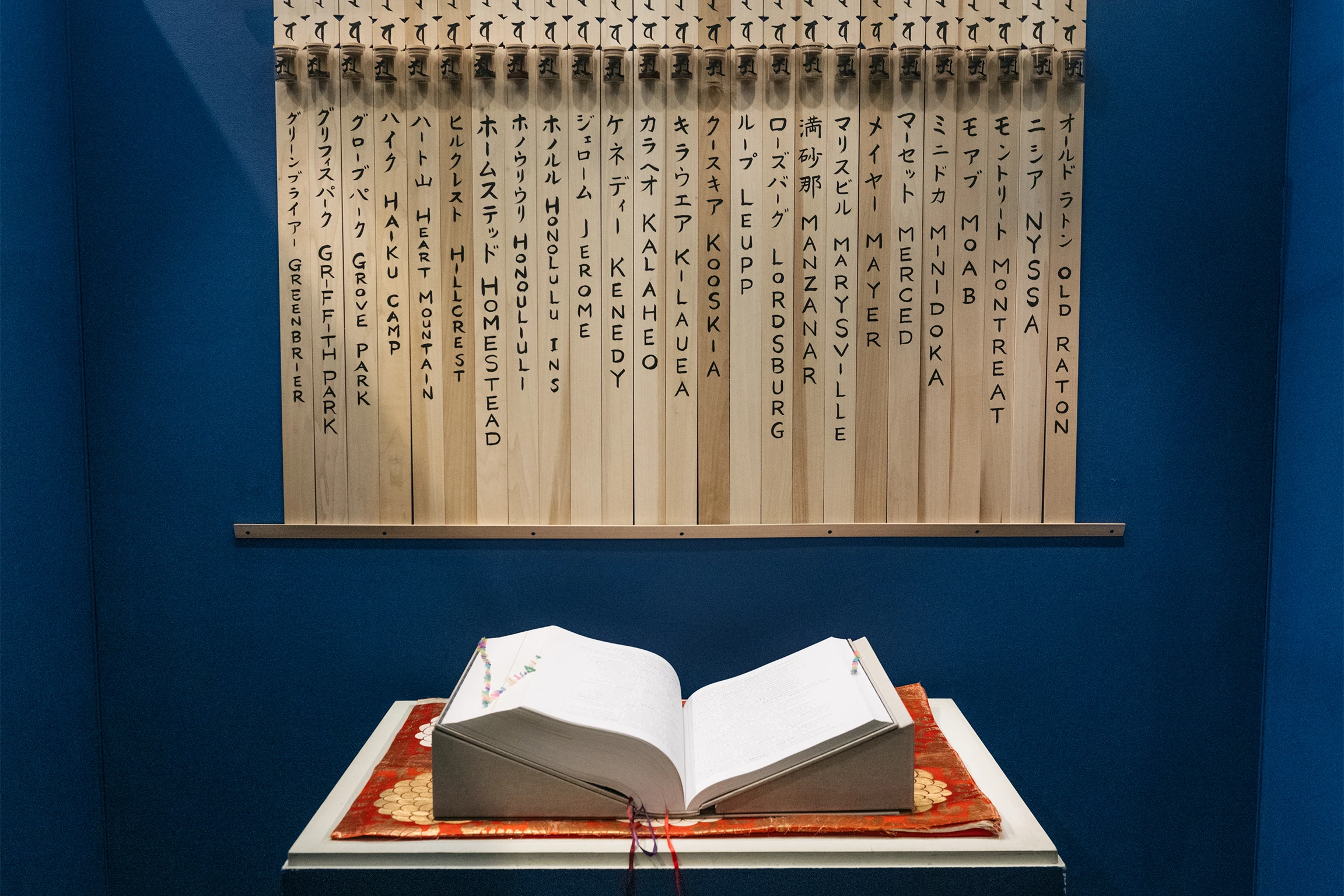 A book sits open on a table in front of a navy blue wall with Japanese writing written on wooden planks