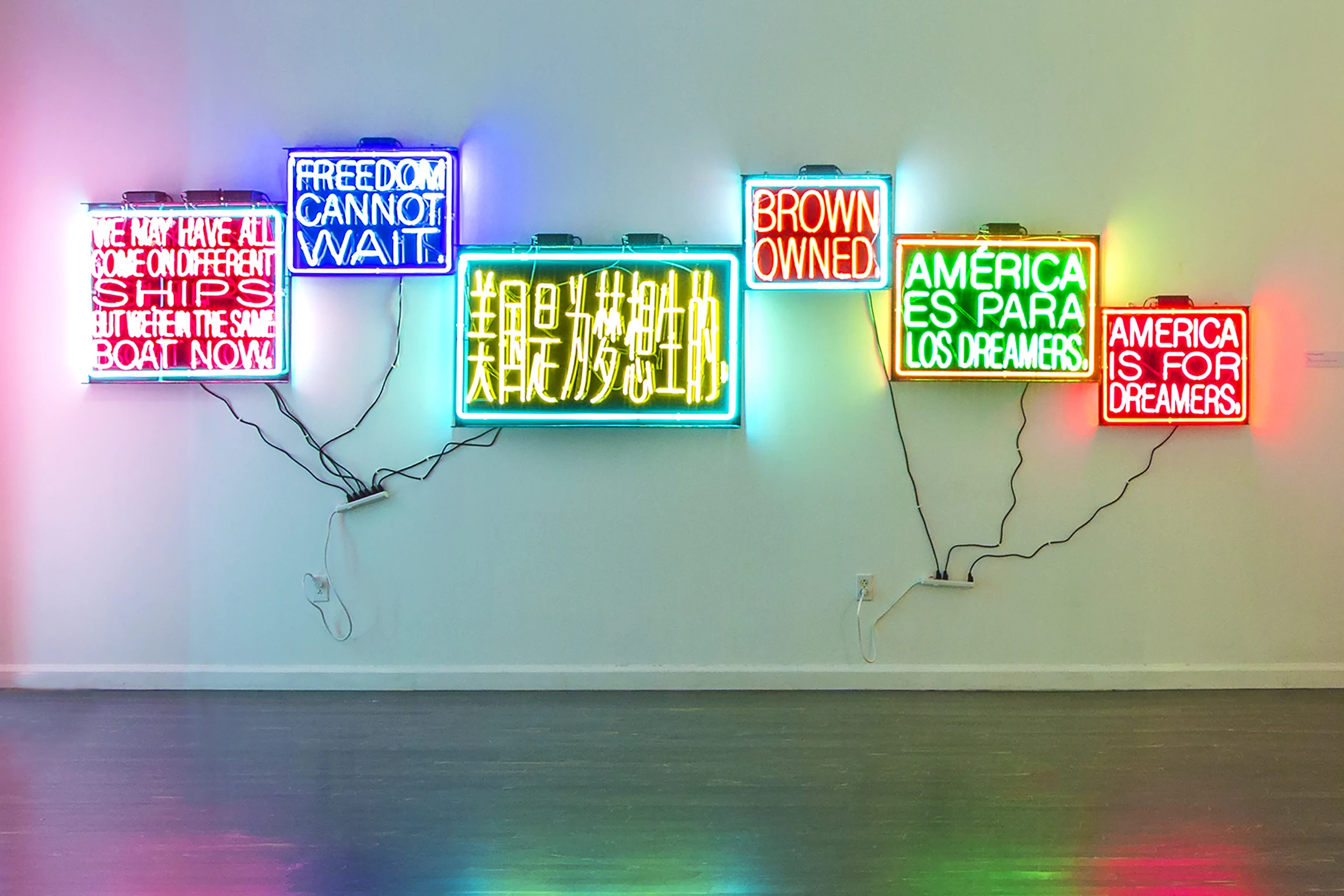Five colorful neon signs hang on the wall with messages that include, "Freedom cannot wait," "Brown owned," and "America is for Dreamers."