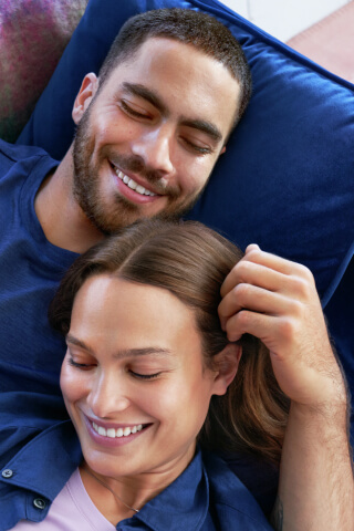 Hombre y mujer acostados en el sofá, su mano sobre su hombro, ambos están sonriendo
