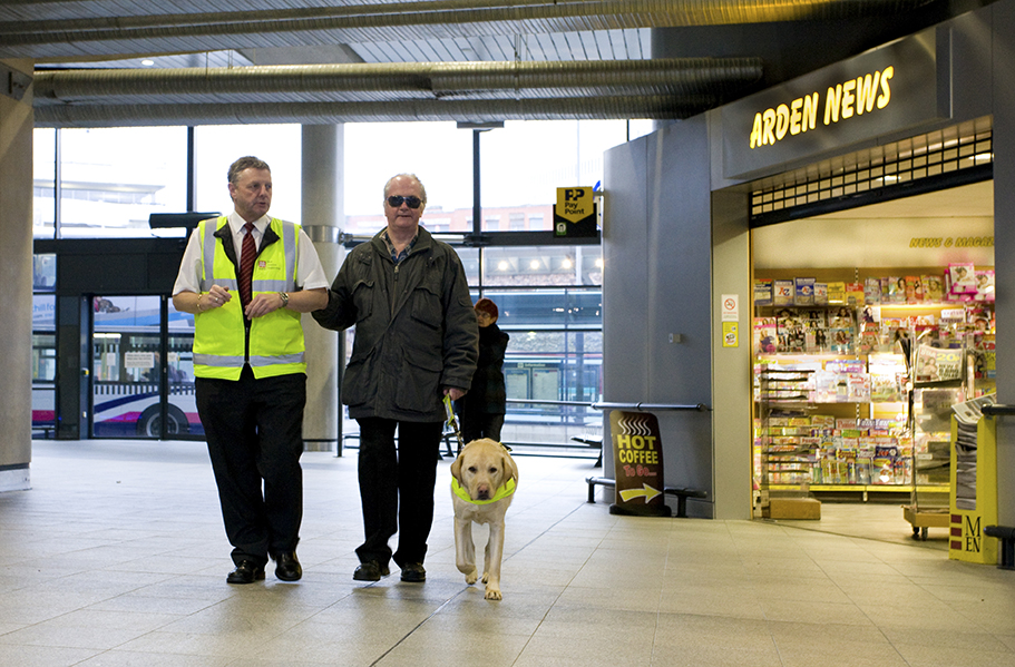 Blind person being supported walking through a bus station