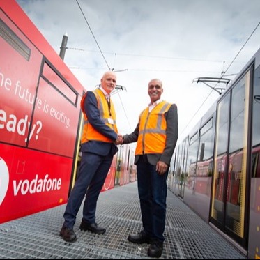 Two men shaking hands next to trams with vodafone advertising on