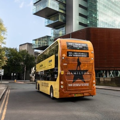 A zero emission bus in greater manchester with an advert of Hamilton on the rear
