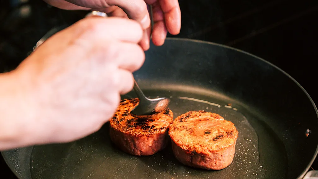 Plant-based beef marbles cooking in pan while chef pours plant-based butter on top.