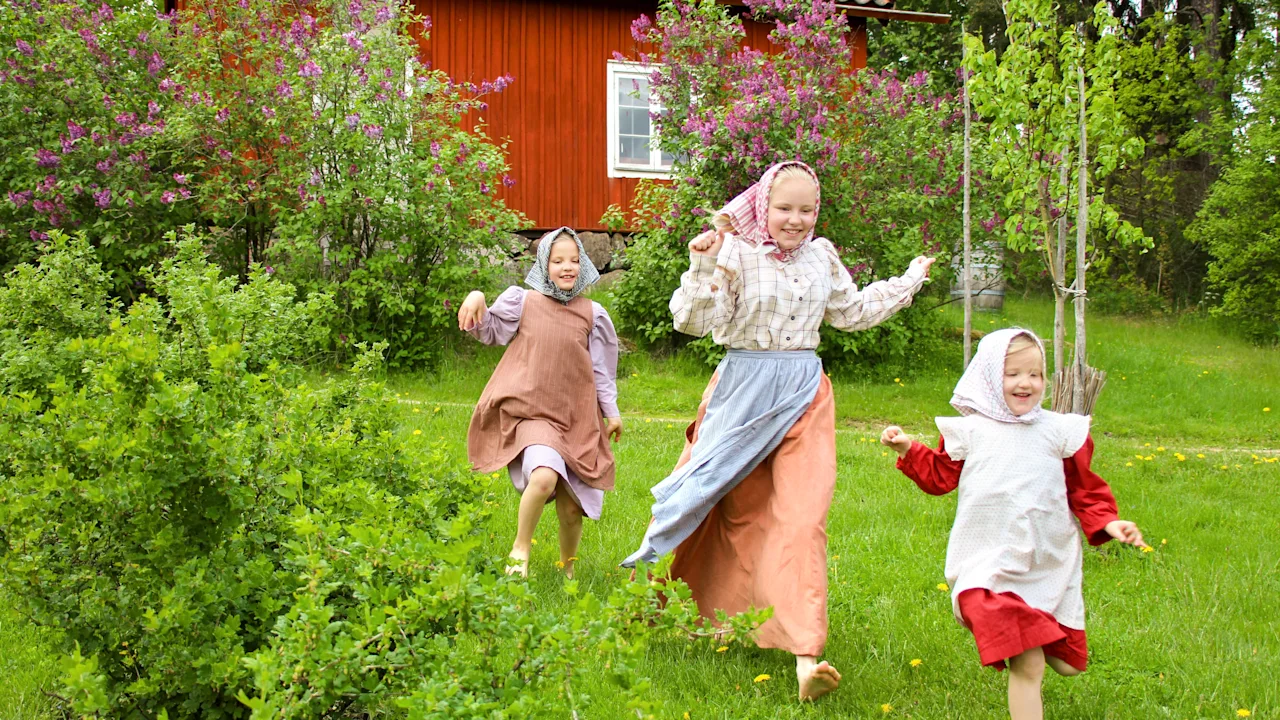 Tre barn i traditionella kläder springer glatt barfota genom ett gräsfält på Vallby Friluftsmuseum Västerås.