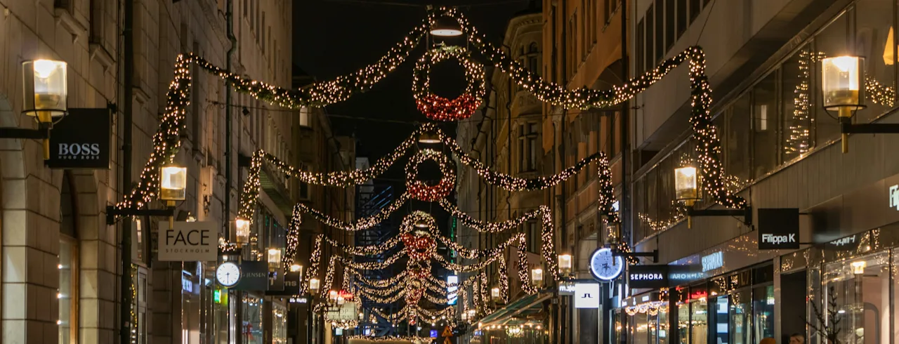 En gågade dekoreret med stemningsfuld julebelysning og kranse der hænger over gaden om aftenen