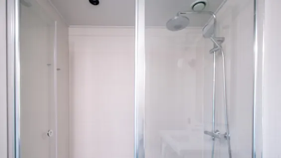 Shower enclosed by glass panels, featuring a round overhead showerhead, in a tiled bathroom with a white sink and light gray flooring.