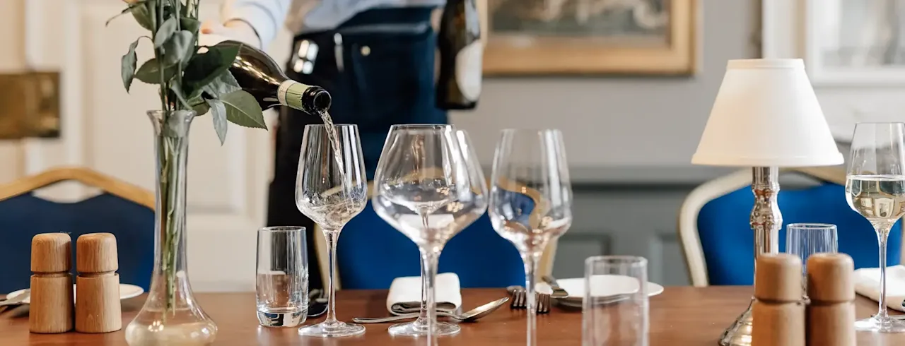 En servitør heller vin i et glass ved et vakkert dekket spisebord på Jørgensens Hotel – Restaurant Eydes.