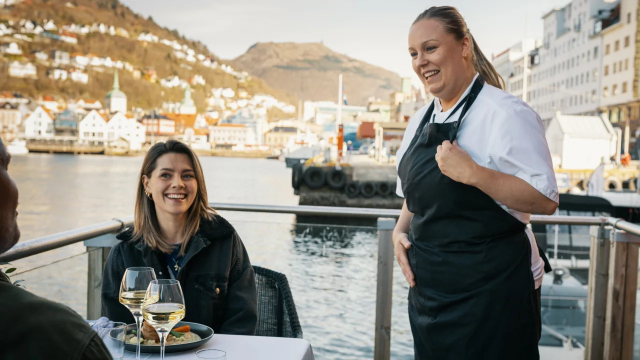 Chef speaking to customers at a restaurant with a beautiful view of Bergen.