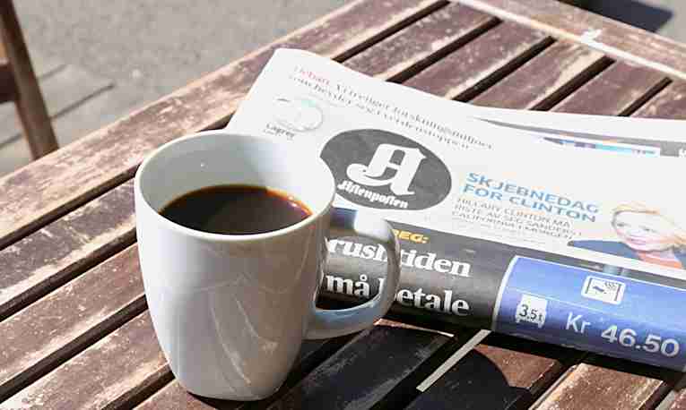 Kaffekopp og Aftenposten på et bord i sola