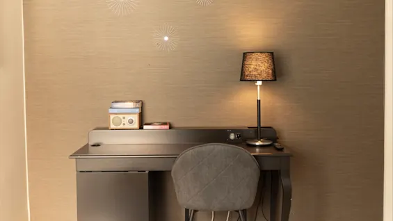 Ett mysigt hotellrums skrivbord med en lampa, böcker och en radio, placerat mot en texturerad vägg med dekorativa stjärnsmällar.