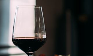 Ett glas rött vin bredvid en tallrik invid ett fönster.
