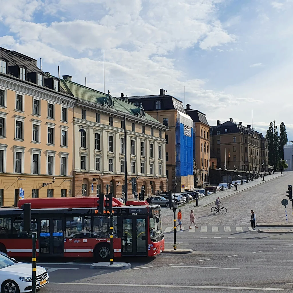 En travel gate i Stockholm med en rød buss, biler og folk som går og sykler, omgitt av historiske bygninger.