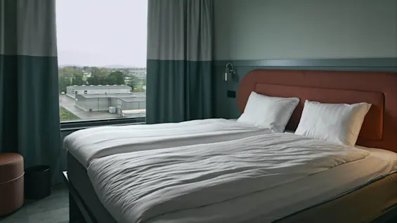 Et moderne hotellrom på Stopover Hotel Falkenberg med to senger, en minimalistisk sengegavl og vindusutsikt over et industriområde.