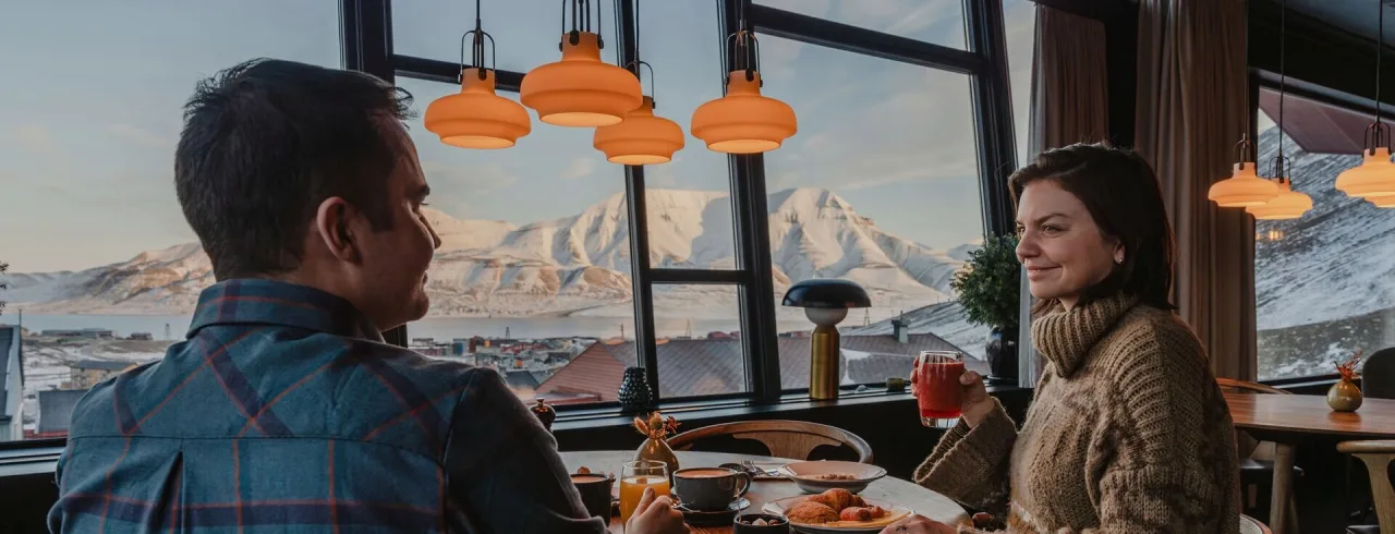 Two people eating breakfast with a magic view at Funken Lodge in Svalbard.