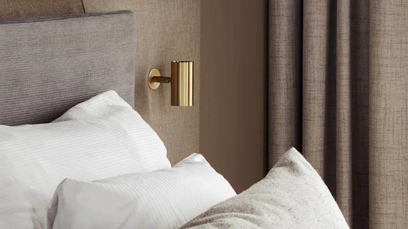 Ett mysigt sovrum med en säng, kuddar och varm belysning från en hängande sfärisk lampa och en väggmonterad lampa. Gardiner är fördragna.